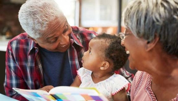 Grandparents Reading Book With Baby Granddaughter At Home