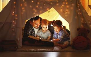happy family father and children reading a book in tent at home